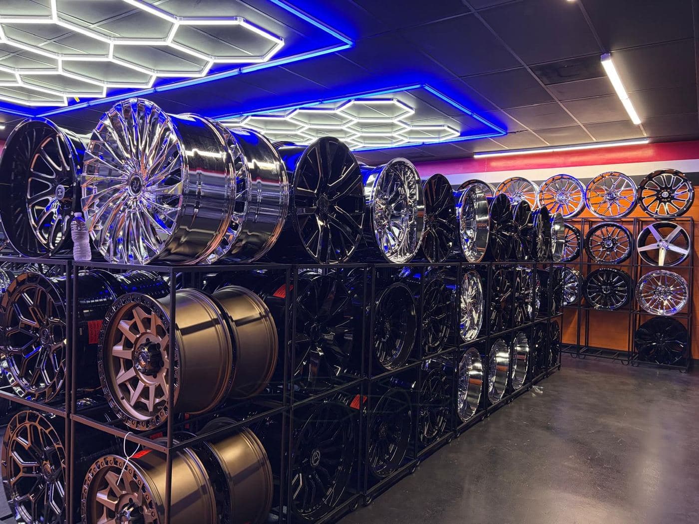 Racks of chrome, black, and bronze wheels under the showroom lights